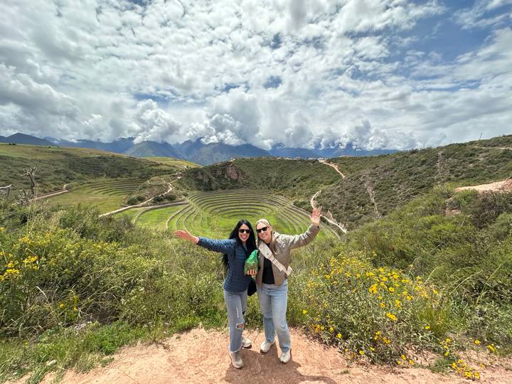 Travellers celebrate with raised arms overlooking the circular agricultural terraces of Moray in the Sacred Valley.