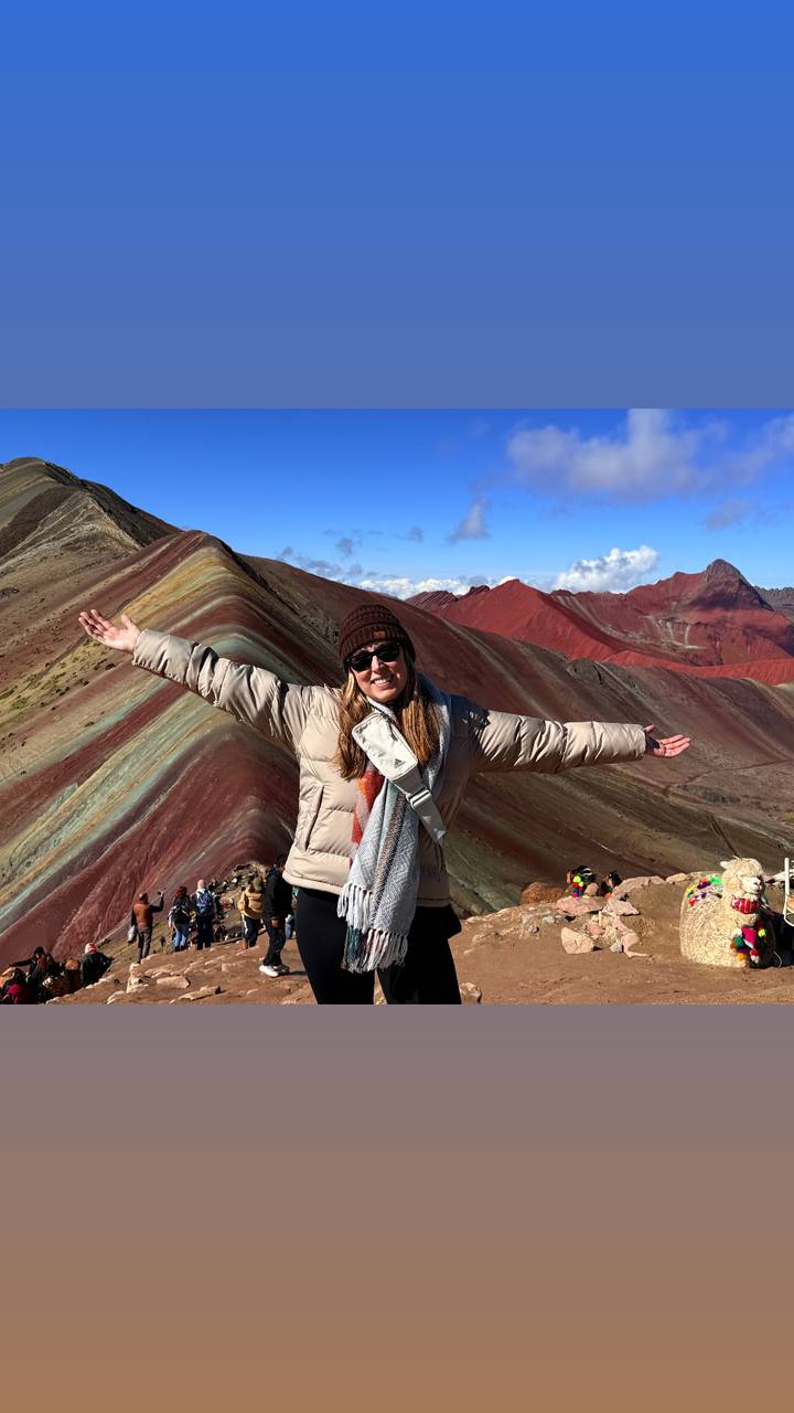 Hiker rejoices with arms spread at the colourful striped slopes of Rainbow Mountain.