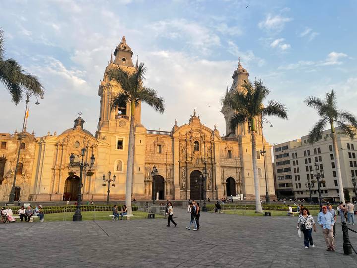 Grand baroque Lima Cathedral dominates Plaza Mayor with palm trees, evening light and locals strolling.