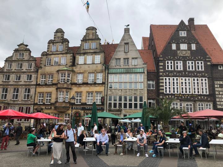 Bustling European town square with historic gabled façades, outdoor umbrellas and crowds.