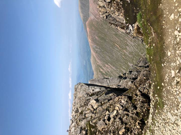Rocky mountain ridge overlooking expansive valleys under a clear blue sky.