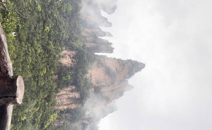 Tall sandstone pinnacles rise from lush forest shrouded in mist within a mountainous landscape.