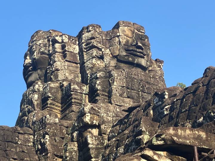 Close-up of weathered stone tower carved with serene smiling faces against blue sky.