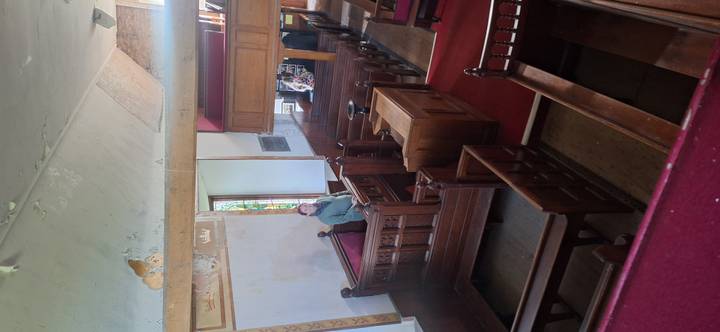 Interior of historic wooden church with visitor standing among polished pews and stained glass.
