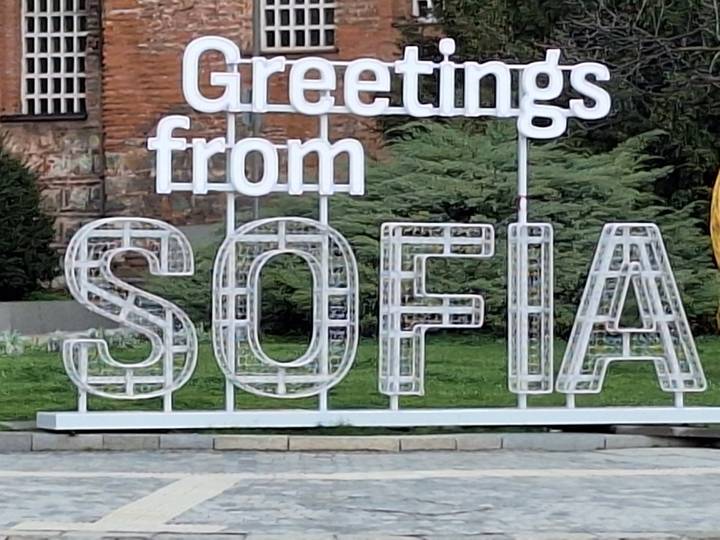 White ‘Greetings from SOFIA’ installation in front of greenery and brick façade.