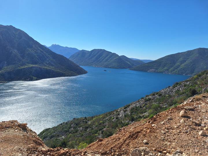 Sparkling deep-blue bay surrounded by high green mountains under a clear sky.