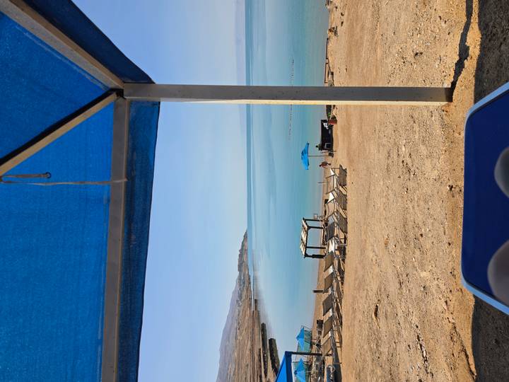 Chill scene of a calm blue sea framed by a beach cabana and lounge chairs.