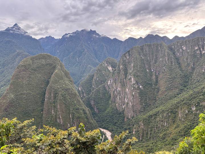 Dramatic Andean peaks blanketed in jungle rise sharply above a winding river far below, under a moody sky.