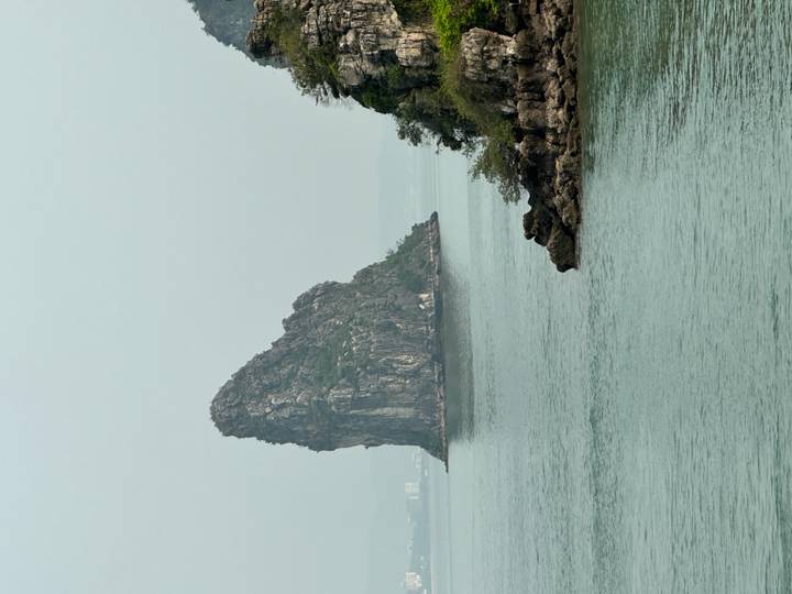 Solitary limestone karst island emerging from calm, hazy waters of Ha Long Bay.