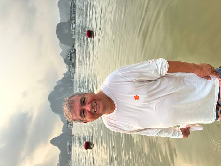 Man standing waist-deep in calm bay waters at sunset with limestone islands and cruise ships in background.