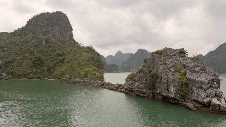 Cloudy day panorama of emerald green water and limestone karst islands in Ha Long Bay.