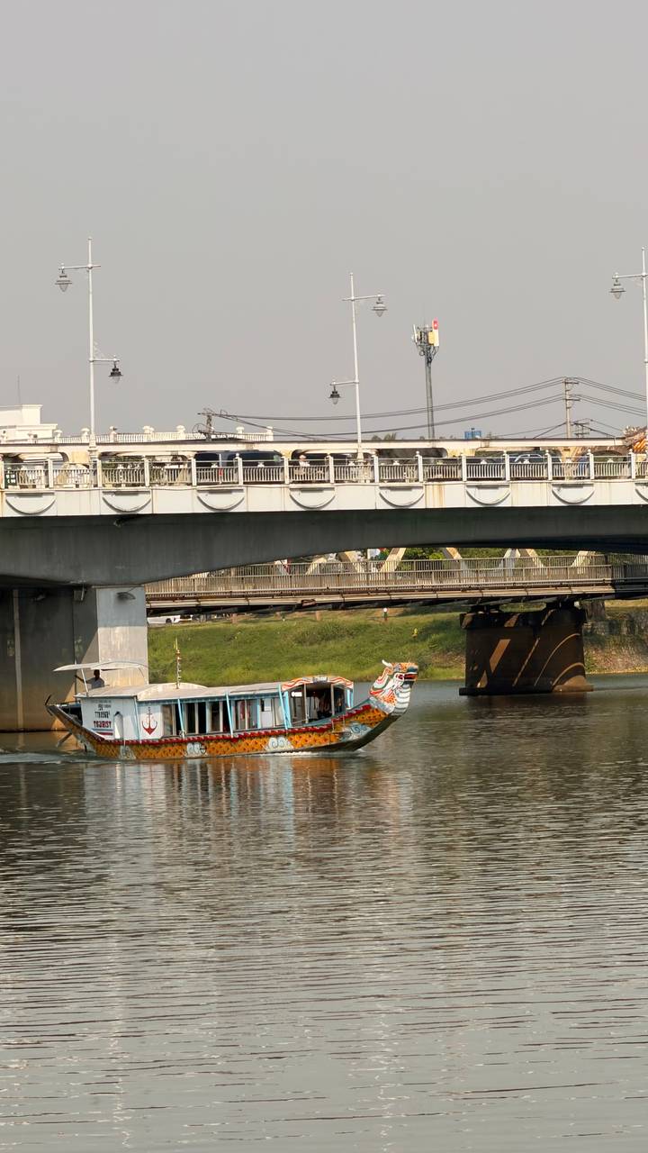 Traditional dragon-painted tourist boat gliding under a concrete bridge on a calm Vietnamese river.