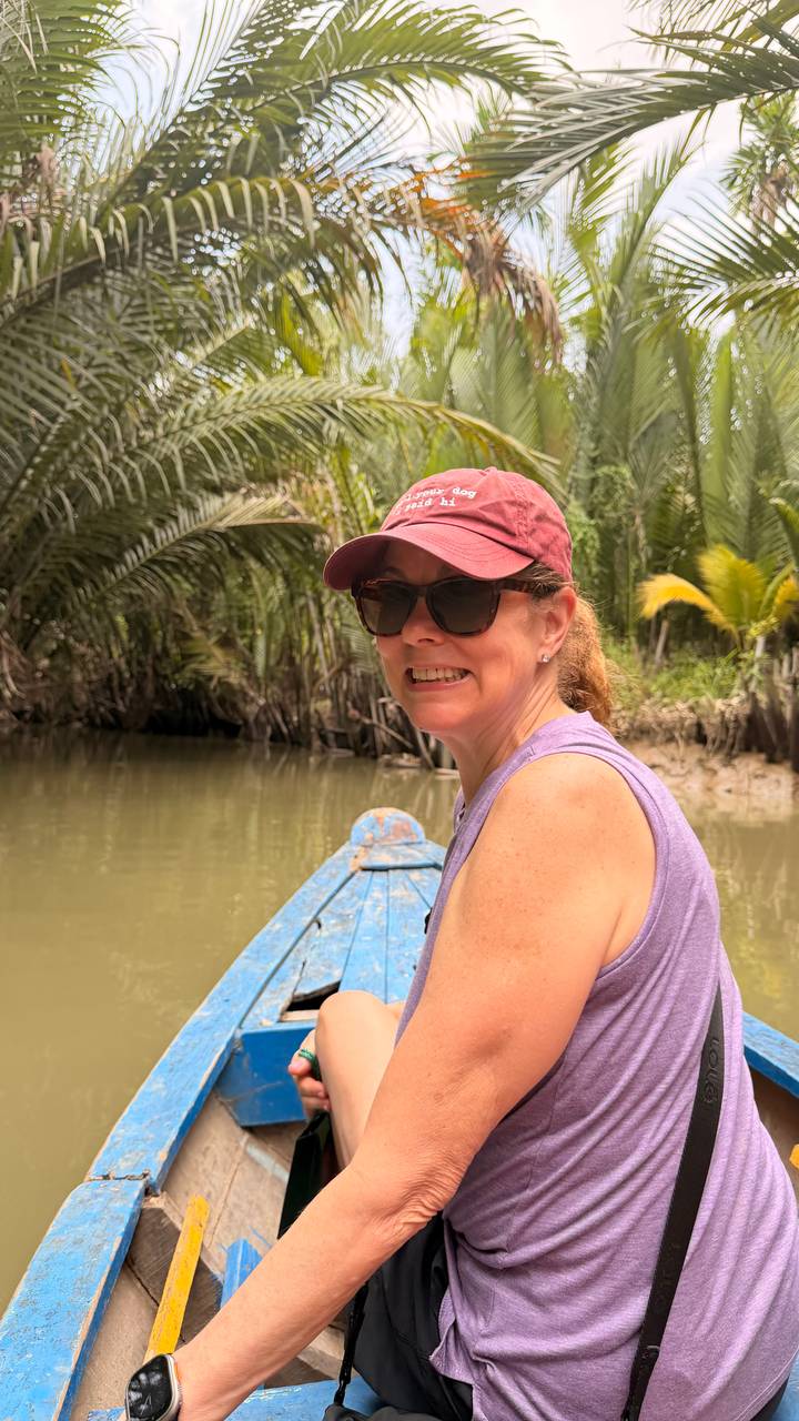 Smiling woman in a small wooden boat navigating a narrow palm-lined canal in the Mekong Delta.