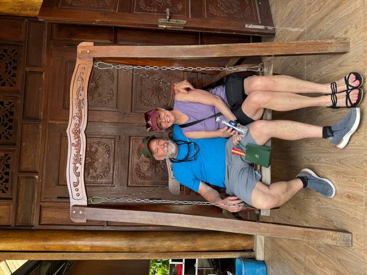 Relaxed couple sitting together on a carved wooden swing in front of ornate Vietnamese doors.