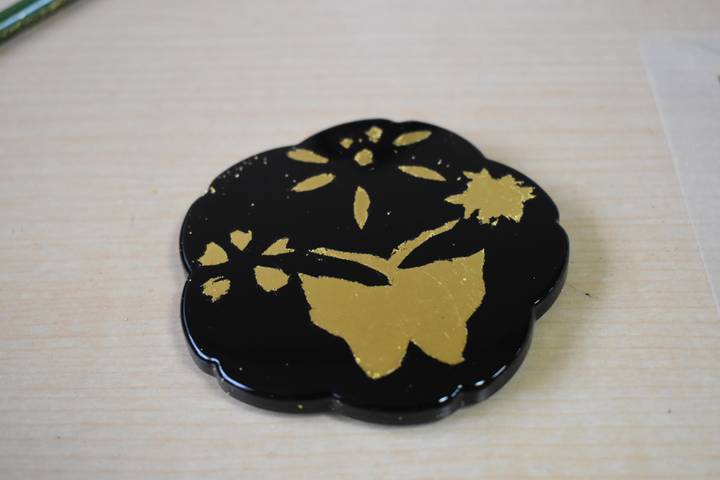 Close-up of a black lacquer coaster decorated with a gold butterfly and flowers.
