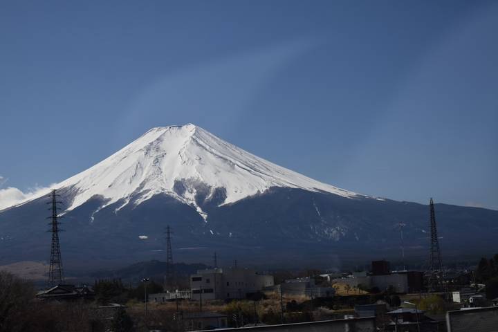Snow-capped Mount Fuji rises above the plains with power lines in the foreground under clear skies.