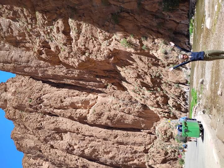Traveler raising arms at the base of towering red rock walls in Todra Gorge.