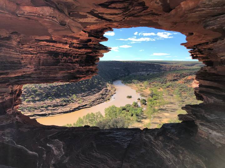 Spectacular rock window frames a winding river valley and rugged canyon landscape under a bright sky.