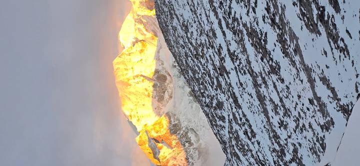Close vertical view of a sun-lit Himalayan peak glowing orange at dusk.