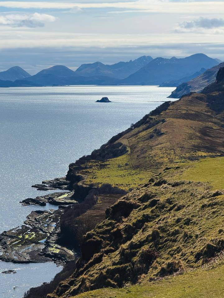 Sun-speckled sea borders a rugged Scottish headland dropping into glittering waters.
