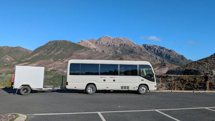 Tour mini-bus with trailer parked at mountain lookout under clear blue sky.