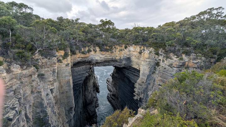Natural sea arch carved into high sandstone cliffs with churning ocean below.