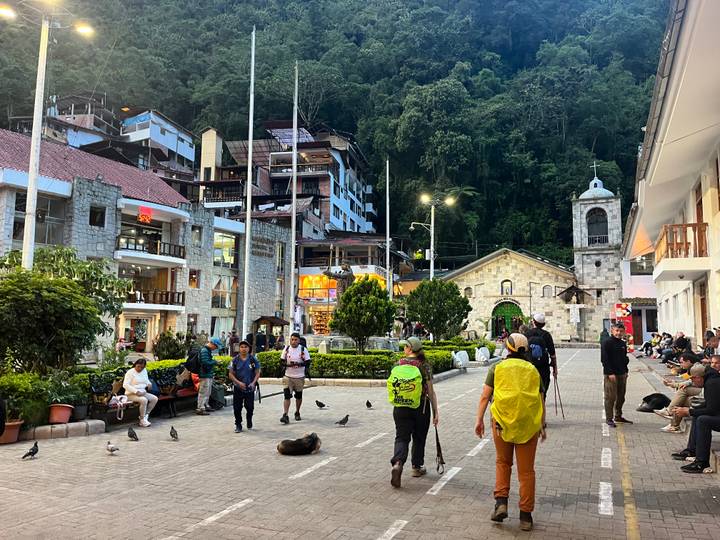 Evening bustle in Aguas Calientes main square with trekkers, pigeons and stone church.