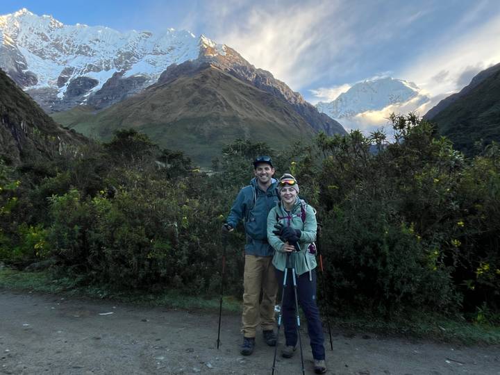 Smiling trekkers posing with snow-covered Andes in background at dawn light.