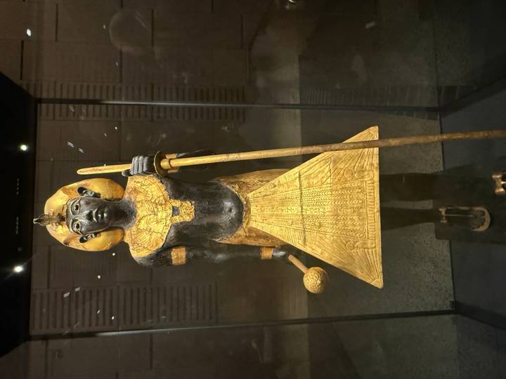 Gold-inlaid wooden statue of Pharaoh displayed in a dimly lit museum case.