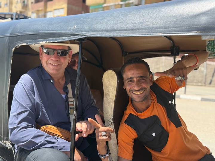 Tourist and tuk-tuk driver smile and flash peace signs inside a motorized rickshaw.