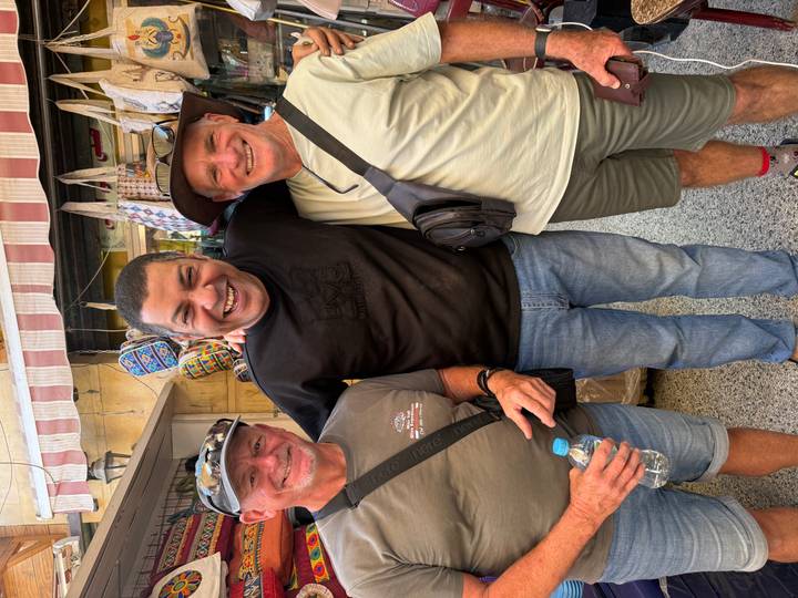 Smiling travelers pose with a friendly local vendor in a bustling market alley.