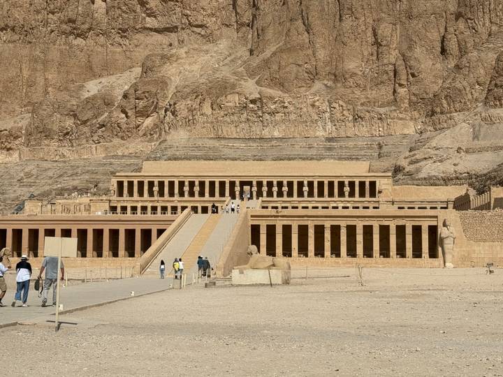 Wide view of the terraced Temple of Hatshepsut set against sheer desert cliffs under a bright sky.