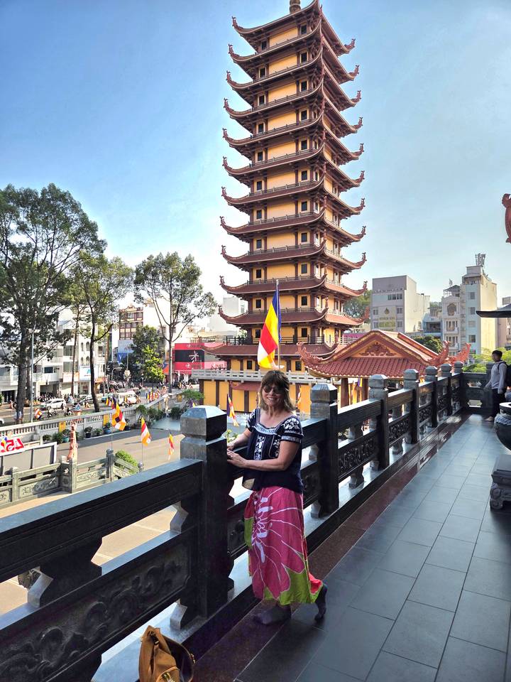 Visitor smiles on a balcony overlooking a busy street and multi-tiered yellow pagoda.