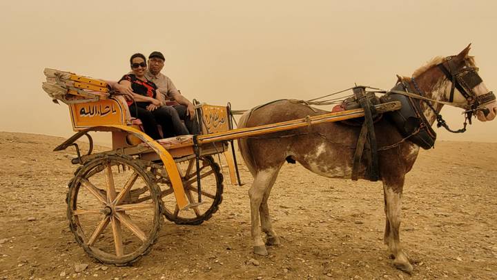 Couple seated on a decorated horse-drawn carriage in the desert near the pyramids.