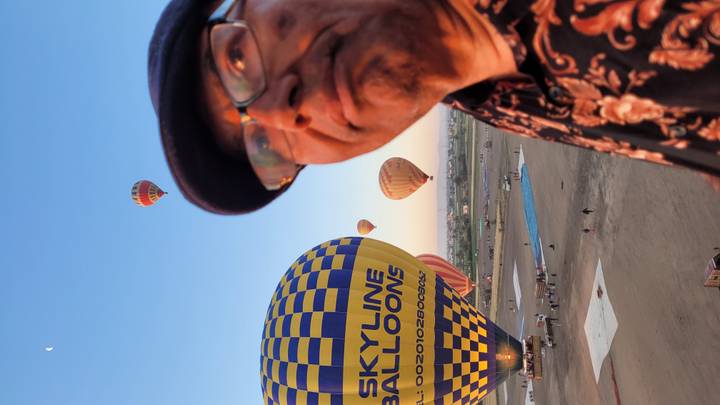 Close-up of a man on a sunrise hot-air-balloon field with colourful balloons ascending in the background.