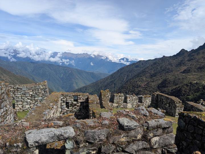 High-altitude Inca stone ruins set against sweeping mountain vistas and clouds.