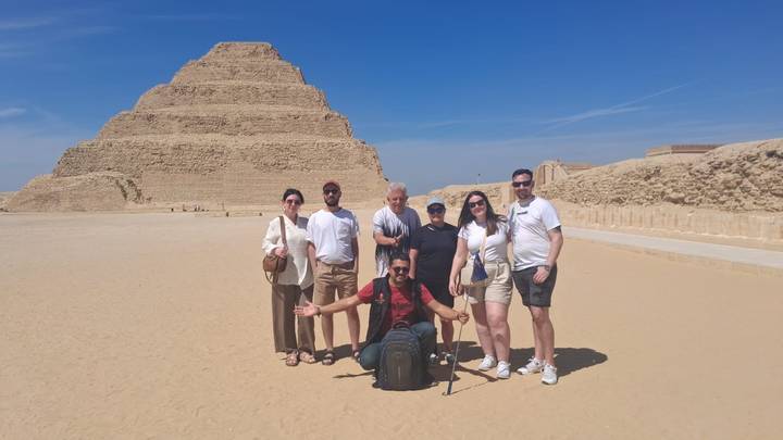Tour group posing in front of the Step Pyramid of Saqqara under a blue desert sky.