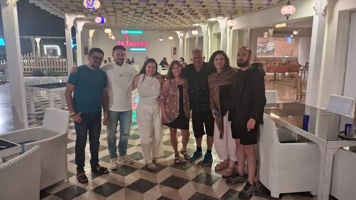 Group of travelers and guide standing on a patterned restaurant floor at night with neon lights.