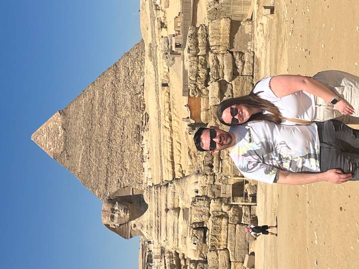Couple standing before the Great Pyramid and Sphinx on a bright desert day.