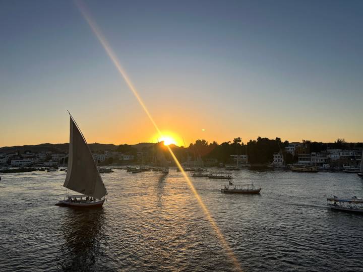 Felucca sailing on the Nile with golden sunset casting reflections on the water.