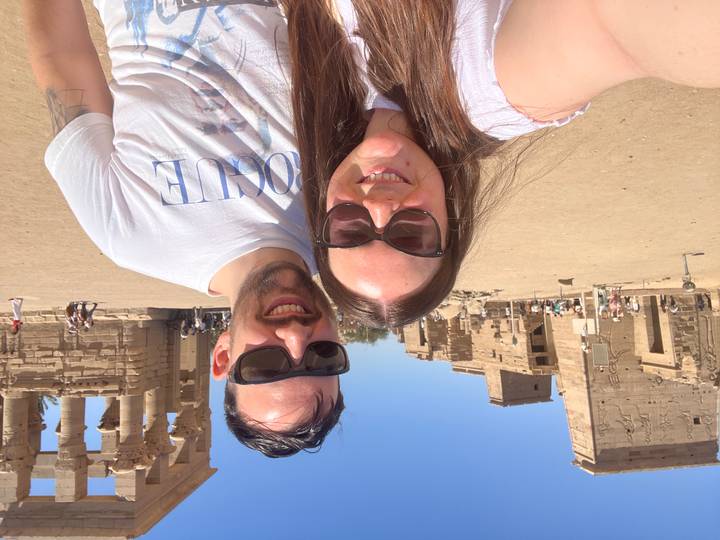 Couple smiling in front of sandstone temple ruins under bright desert sun.