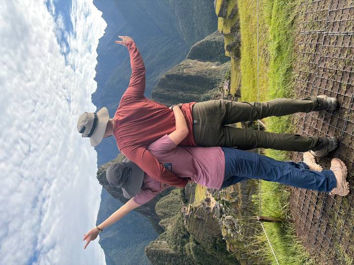 Hiking couple embracing while overlooking Machu Picchu ruins and surrounding mountains.