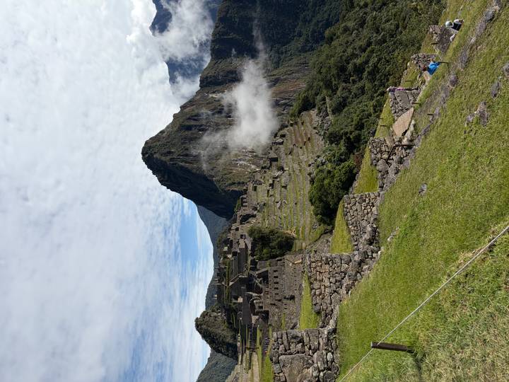 Machu Picchu terraces and ruins partially shrouded in morning mist with blue mountains beyond.