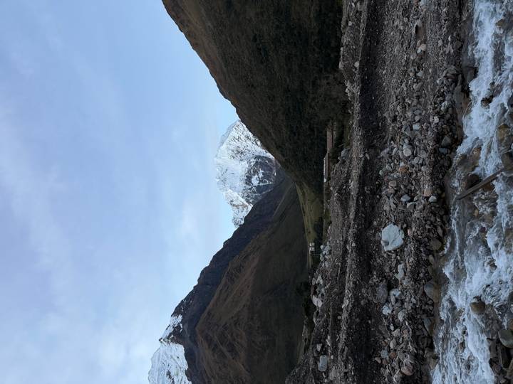 Snow-capped Andean peak towering above a V-shaped valley with a rocky river in the foreground.