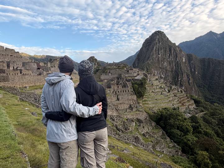 A couple dressed in trekking gear embrace while admiring the stone terraces of Machu Picchu at dawn.