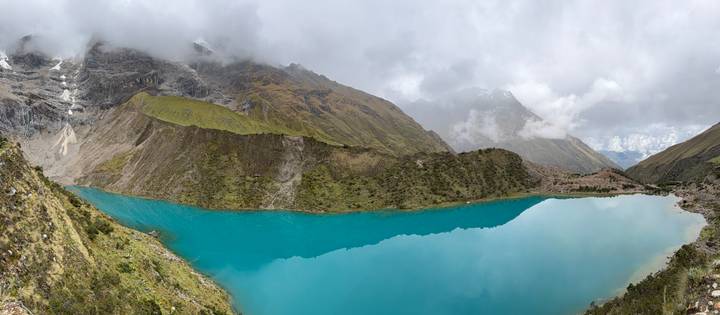 Panoramic view of an intense blue alpine lake ringed by steep, mist-shrouded Andes slopes.