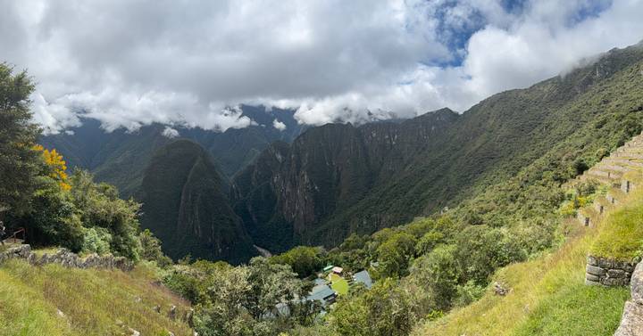 Lush river valley and distant peaks viewed from the terraces near Machu Picchu on a partly cloudy day.
