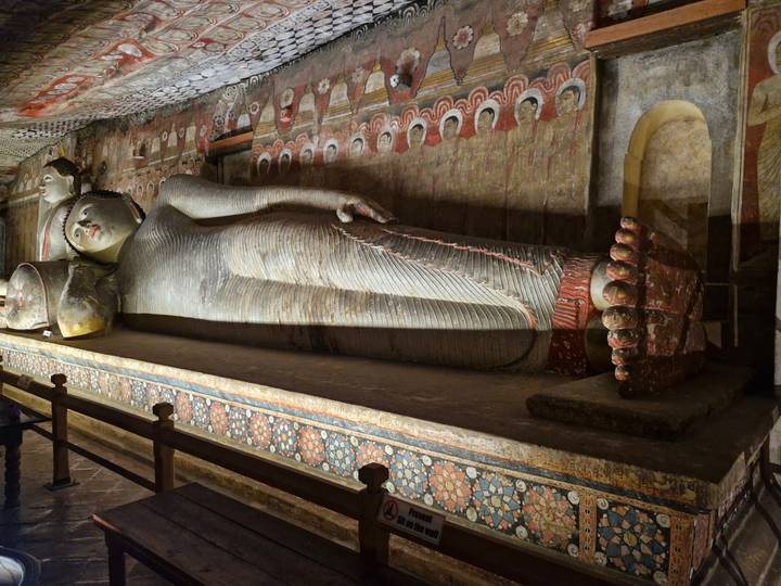 An ancient reclining Buddha statue lies within a richly painted cave temple hall.