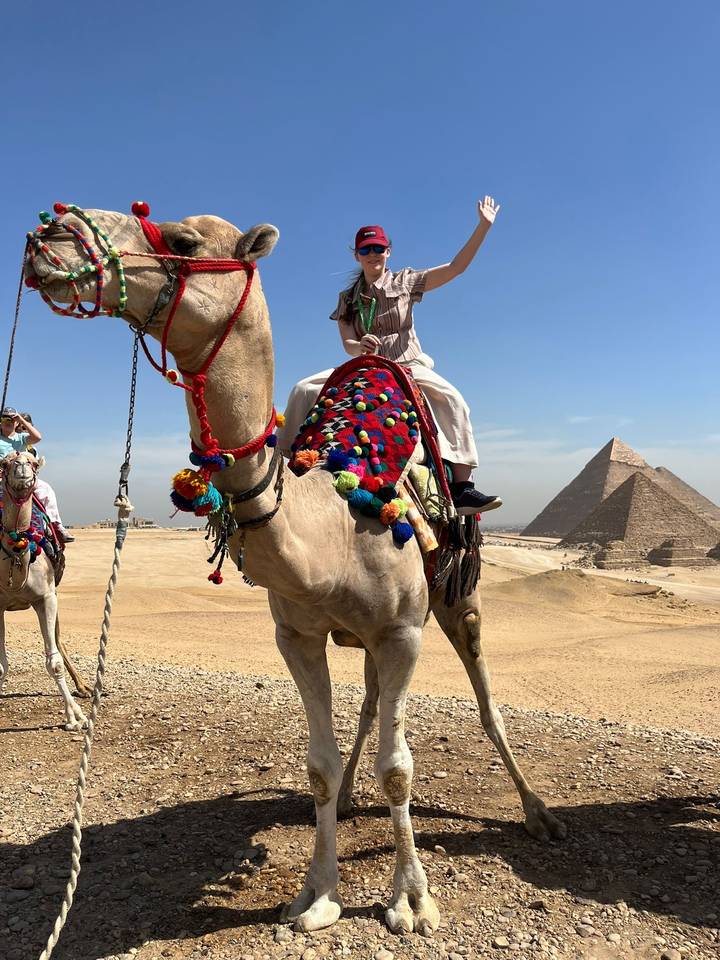 Decorated camel with riders in colourful attire standing before the pyramids on a sunny desert day