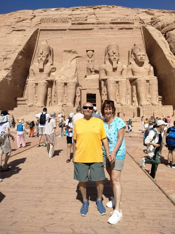 Tourists posing in front of the giant seated statues of Abu Simbel temple on a bright day